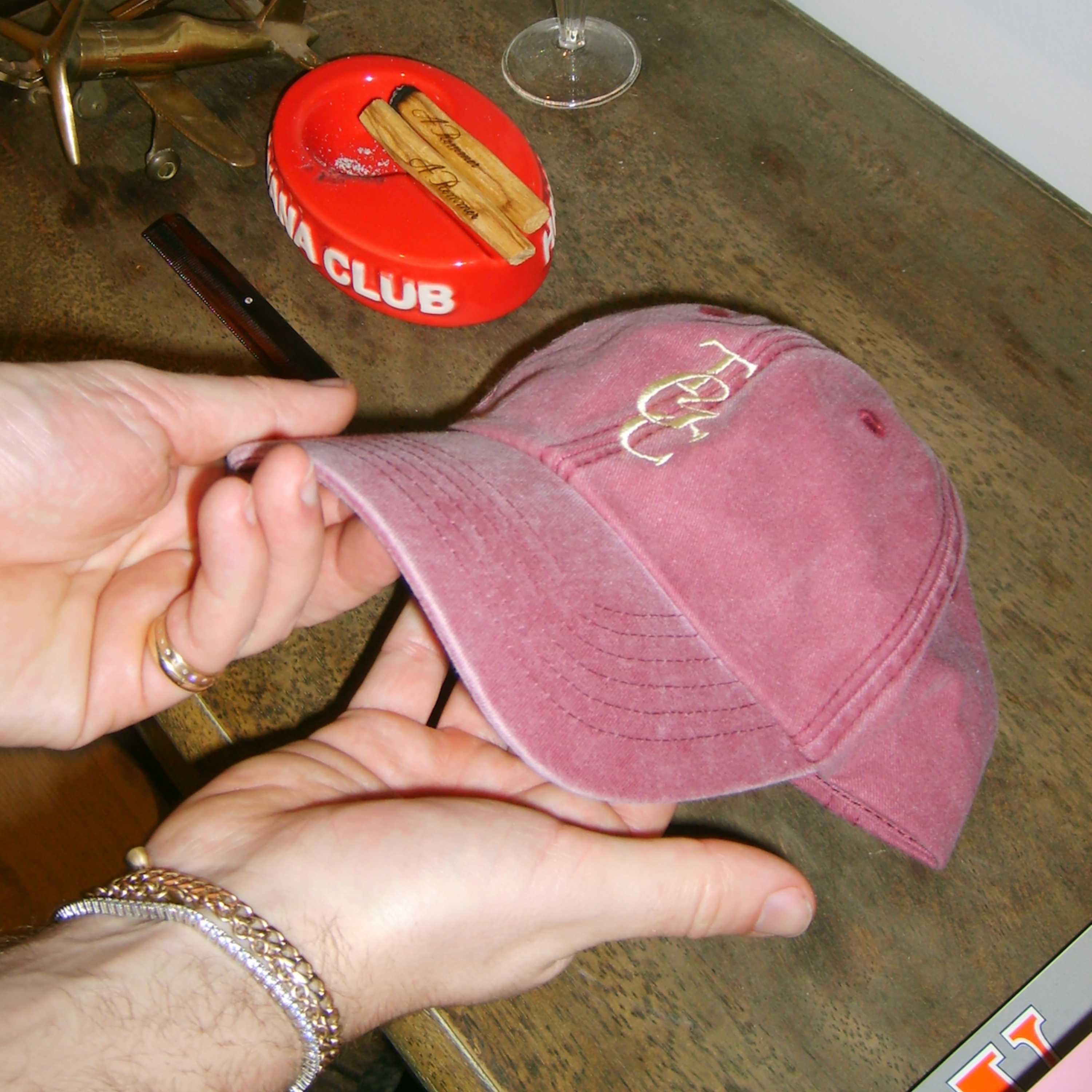 Burgundy TGC Cap being held on table. 