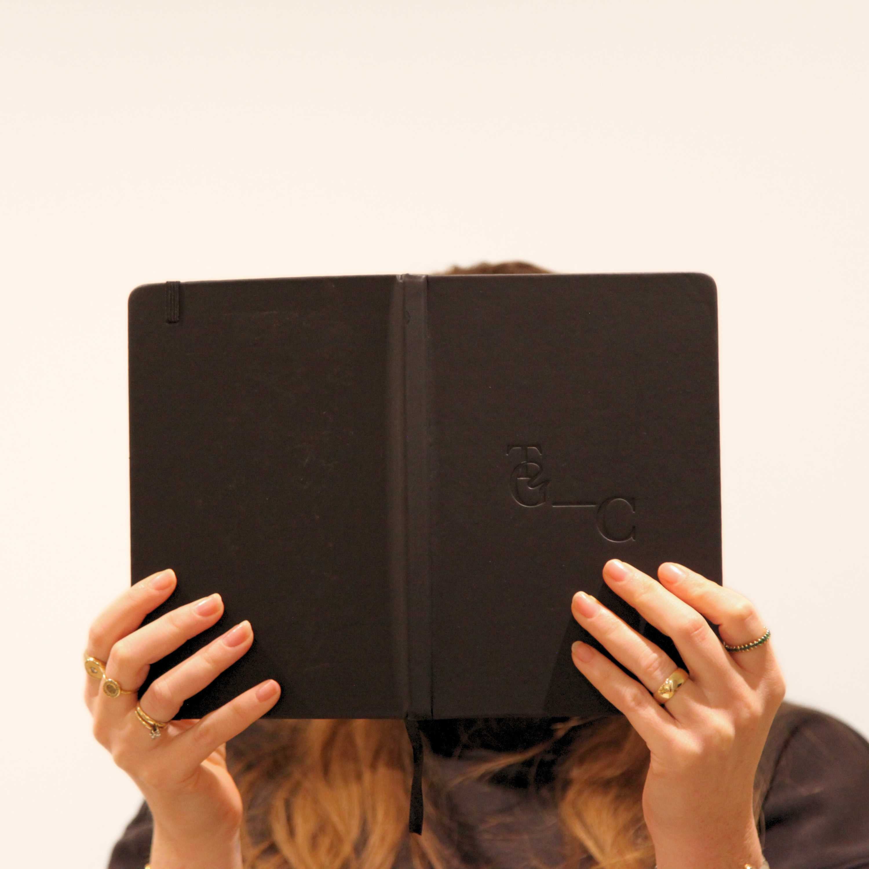 Person holding a black leather-bound book with TGC branding against a plain background