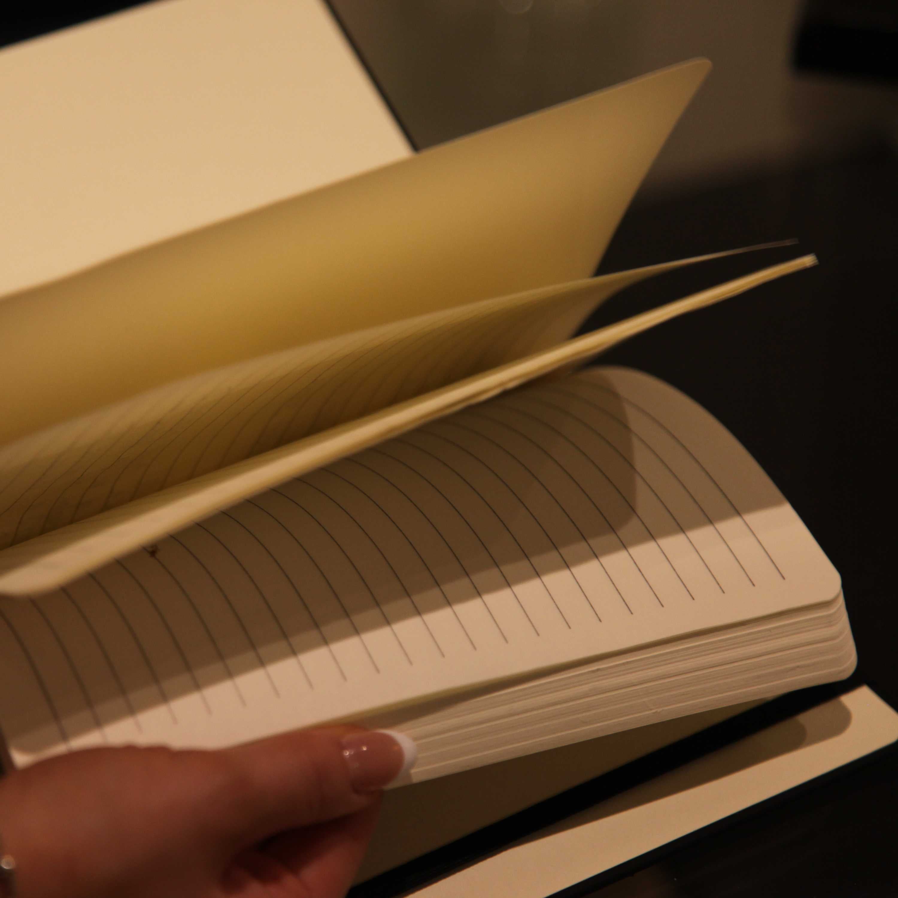 Open notebook with lined pages held by a hand against a dark background