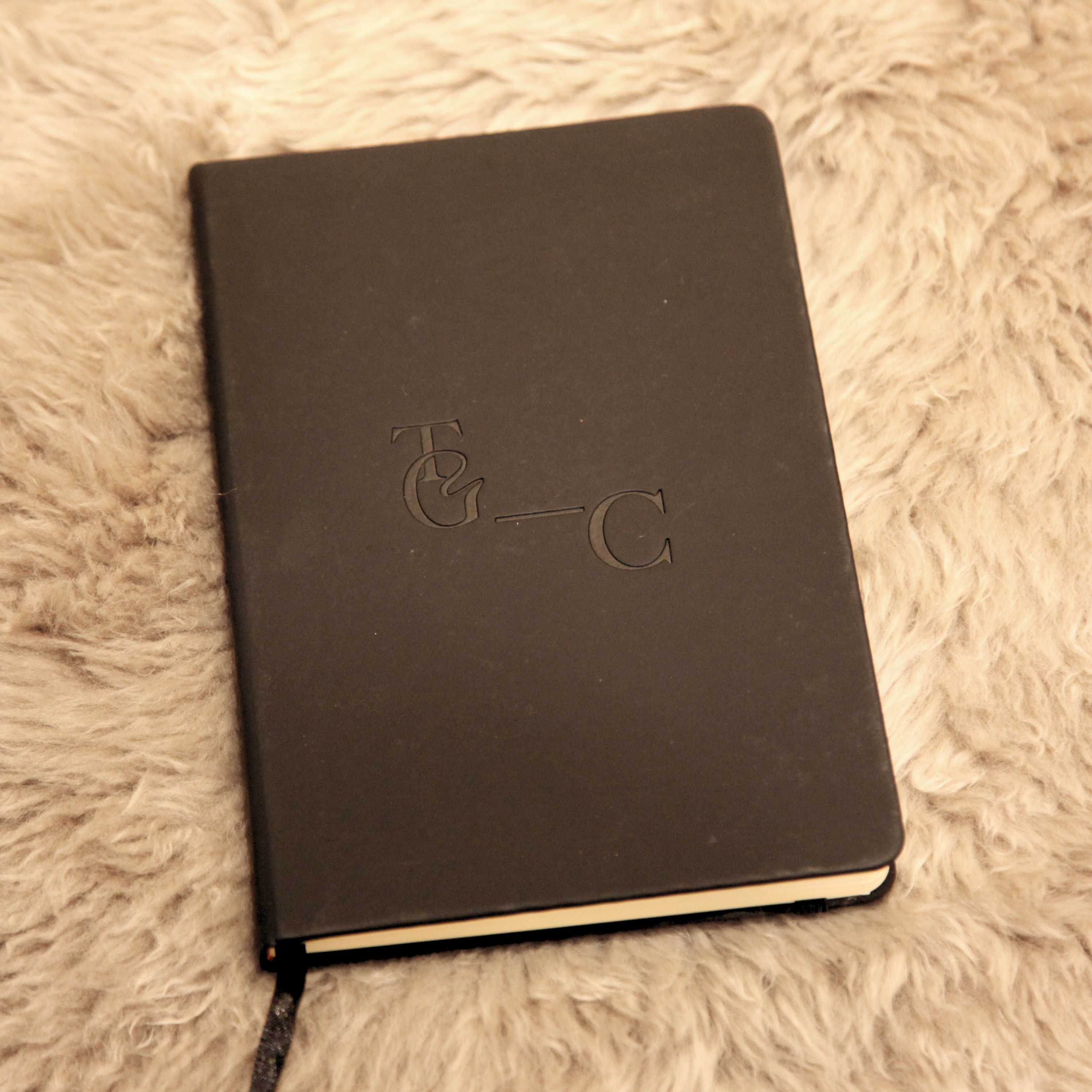 Black notebook with embossed TGC logo on a beige textured surface