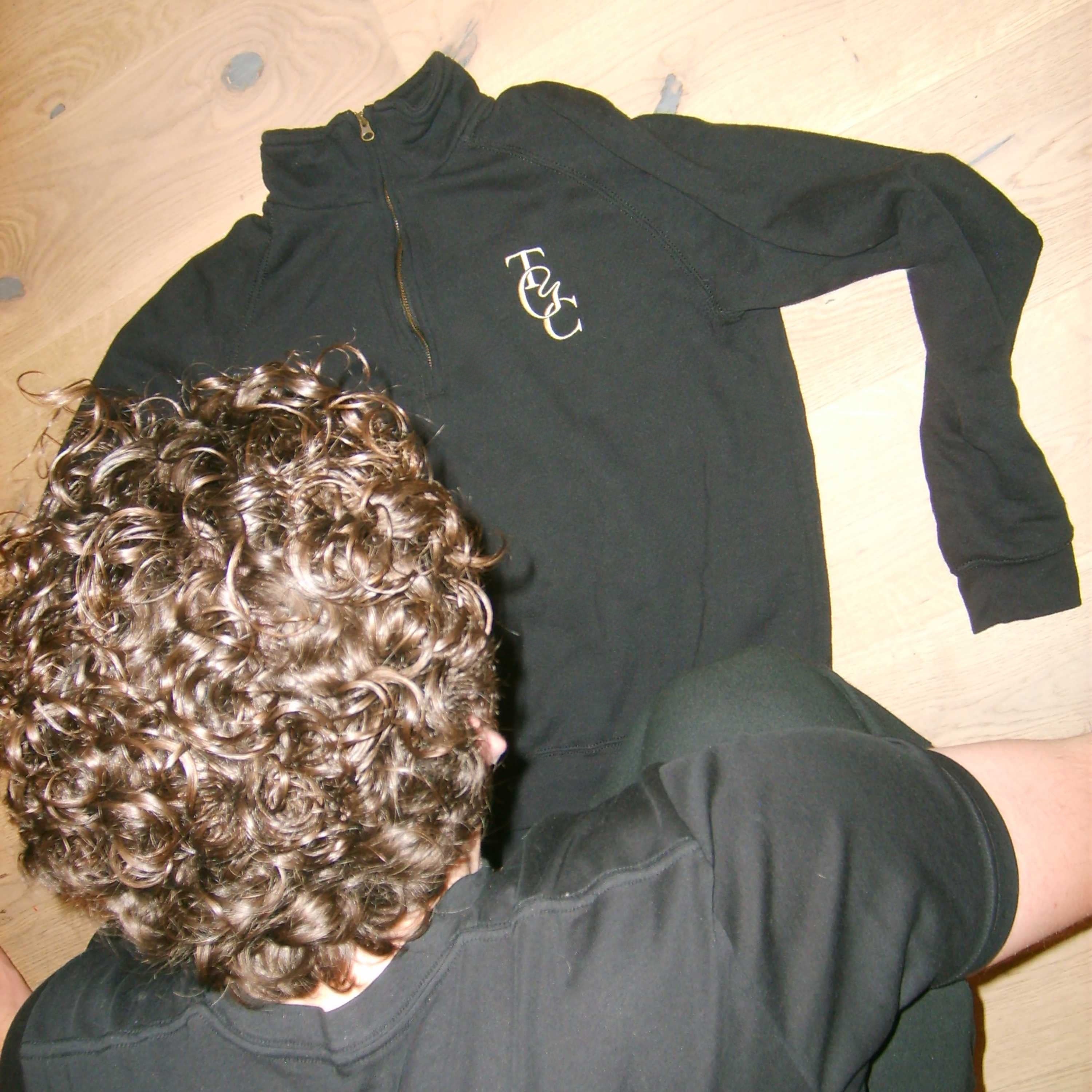 Black long-sleeve quarter zip hoodie with TGC logo on a beige surface