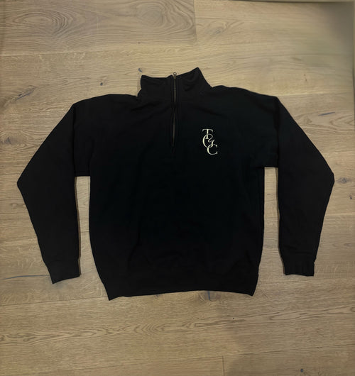 Black quarter-zip sweatshirt with TGC logo on a wooden floor
